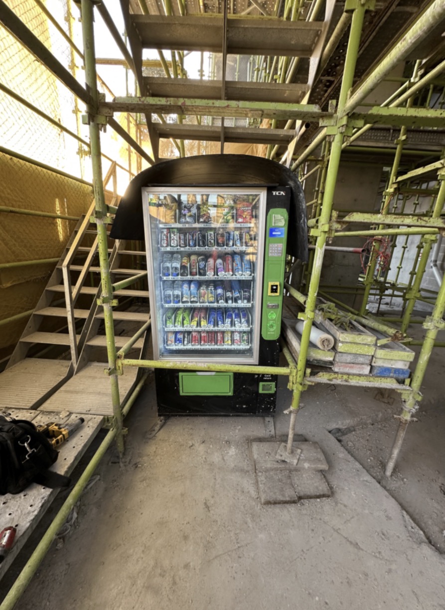 Stocked Vendor Bros. vending machine installed under scaffolding on a construction site